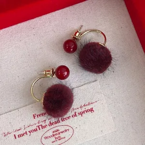 Vintage burgundy plush ball earrings with gold accents on a textured fabric backdrop