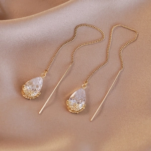 Detailed macro view of long drop earrings with white zircon on elegant silk fabric