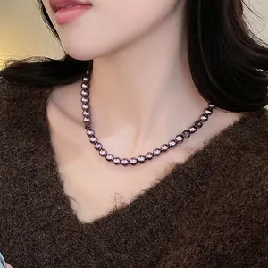 Primo piano della collana di perle di vetro viola scuro lucido su maglione marrone