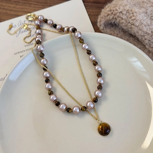 Détail macro du collier superposé en œil de tigre et perles sur assiette céramique