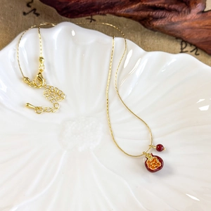 Macro detail of gold pomegranate pendant necklace with red crystals on a white plate