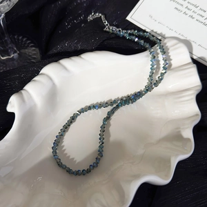 Close-up of iridescent blue-green crystal beaded necklace in a white shell dish