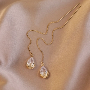 Detailed view of gold tassel earrings with pear-cut zircon on champagne satin fabric