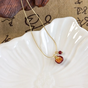 Macro shot of gold pomegranate necklace pendant with red seeds on ceramic tray