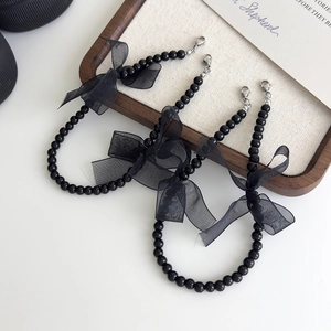 Détail de nœud en dentelle noire avec chaîne de perles et fermoir argenté pour chaussures