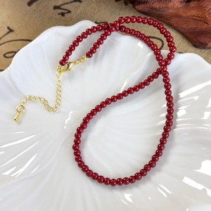 Detail of red pomegranate beaded necklace with adjustable gold lobster clasp on white tray