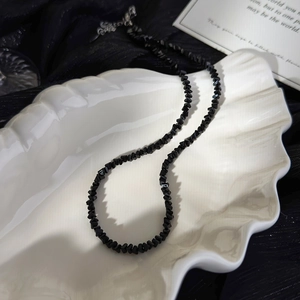 Macro detail of black crystal bead necklace with silver clasp on white shell plate