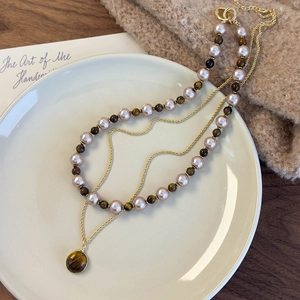 Détail d'un collier double couche avec pierres oeil de tigre et perles sur un plateau chic