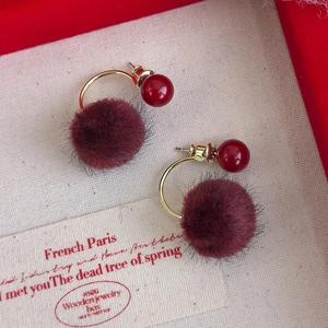 Macro detail of red faux fur ball earrings with polished gold accents on jewelry box