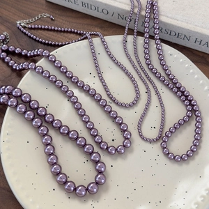 Eleganti collane di perle di vetro viola in varie dimensioni su un piatto ceramico