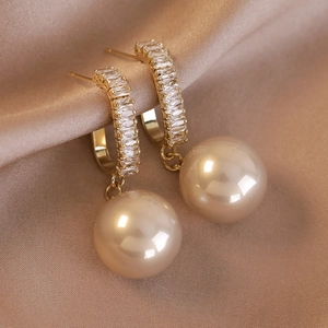 Dettaglio macro di orecchini pendenti placcati in oro con zirconi e perle champagne