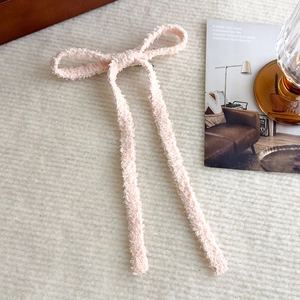 Dettaglio del fermaglio a fiocco rosa in peluche con lunghi nastri su sfondo accogliente