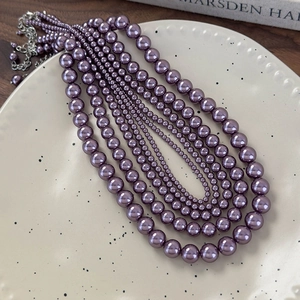 Dettaglio di cinque collane di perle di vetro viola in varie dimensioni su un piatto ceramico