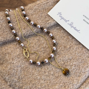 Détail d'un collier doré multicouche avec pierres œil-de-tigre et perles sur tissu doux