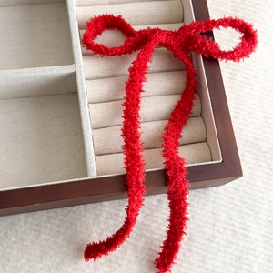 Dettaglio ravvicinato di un fermaglio per capelli a fiocco rosso in peluche su scatola di legno