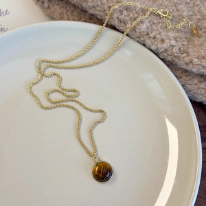 Détail du collier chaîne torsadée dorée avec pendentif œil de tigre sur plateau blanc