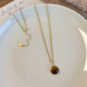 Détail d'un pendentif en œil de tigre sur collier doré posé sur une assiette blanche
