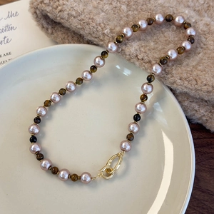 Détail d'un collier de perles en œil de tigre et perles sur plateau en céramique