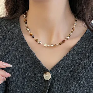 Gros plan d'un collier de perles en œil de tigre sur un modèle en pull gris