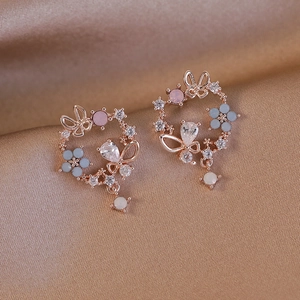 Macro detail of butterfly and flower earrings with zircon on champagne silk background