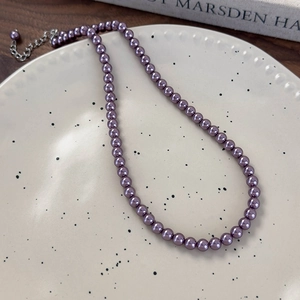 Primo piano della collana di perle viola con chiusura a moschettone su piatto ceramica