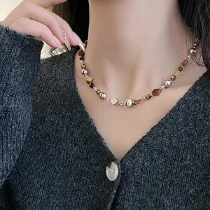 Détail du collier de perles en œil de tigre porté sur un pull en maille grise