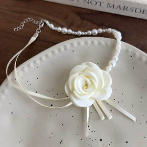 Dettaglio della collana girocollo con perle e camelia con nastro su piatto in ceramica