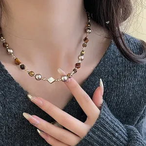 Détail d'un collier en œil de tigre et perles avec un pendentif losange en nacre