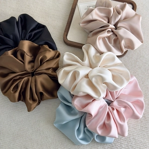 Detailed view of six glossy satin scrunchies in varied colors on a wooden tray