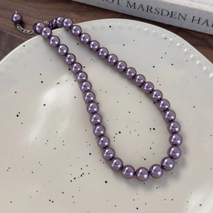 Dettaglio di collana in perle di vetro viola con catena regolabile su piatto di ceramica