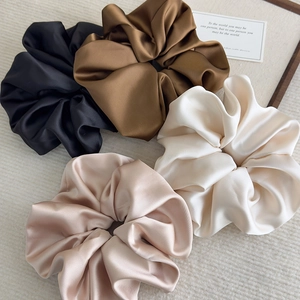 Flat lay of four glossy satin scrunchies in neutral tones on a beige knit background