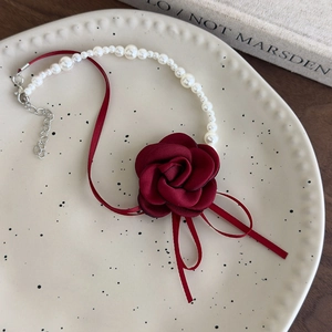 Dettaglio della collana choker con camelia rossa e perle su un piatto in ceramica vintage