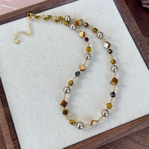 Détail du collier en œil de tigre et perles avec pendentif cœur sur fond de toile de jute