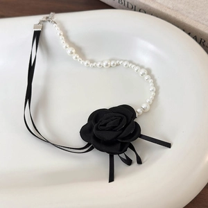 Dettaglio girocollo con rosa di raso nero, perle bianche e nastri su un piatto