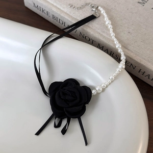 Dettaglio della collana di perle camelia con nastro nero e perle bianche su un piatto