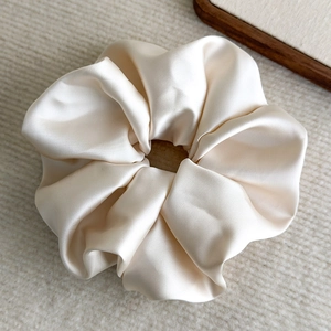 Macro detail of high-gloss cream satin fabric texture on an oversized scrunchie
