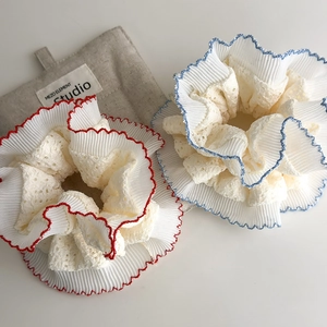 Close-up of beige lace scrunchies with red and blue wavy stitched edges on fabric background