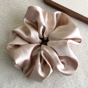 Macro detail of glossy satin oversized scrunchie in champagne gold on textured fabric