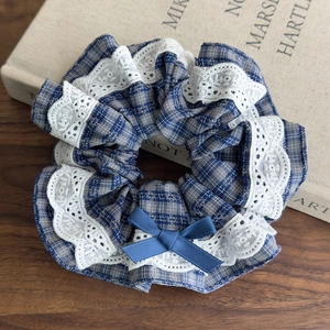 Detail view of plaid fabric scrunchie with white lace trim and dark blue ribbon bow