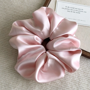 Close-up of a soft pink satin scrunchie with glossy texture and elegant folds
