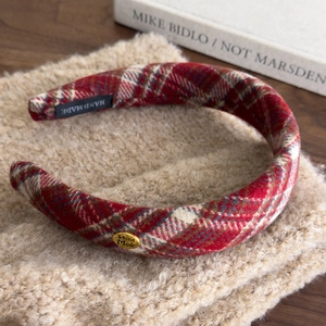 Red plaid headband with gold metal handmade logo for women over a soft beige background