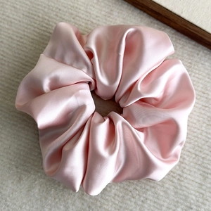Detail of light pink satin scrunchie showing glossy silk texture and elegant fabric folds
