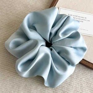 Close-up of a large ice blue satin scrunchie showing glossy texture and rich pleats