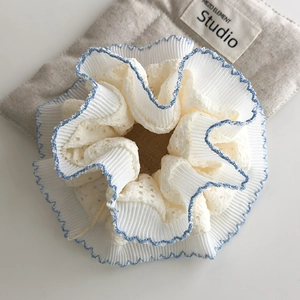 Detailed close-up of cream lace scrunchie with blue scalloped edges and pleated texture