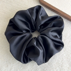 Close-up of a large black satin scrunchie with silky luster on a beige textured rug