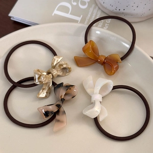 Close-up of acetate bow hair ties in marble, amber, and pearl finishes on a tray