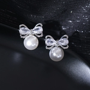 Macro detail of silver bow earrings with zircon stones and a lustrous round pearl charm