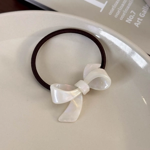 Detail of elegant white acetate bow hair tie with pearlescent finish on a ceramic plate