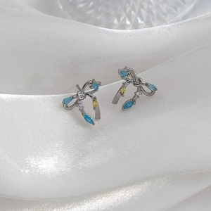Détail des boucles d'oreilles en nœud avec zircons bleus et jaunes sur tissu de soie blanc