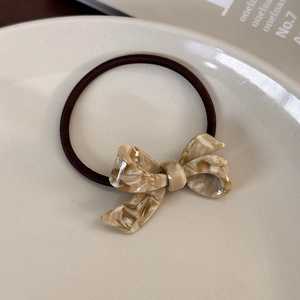 Detail of beige marble acetate bow hair tie with premium texture on a white dish